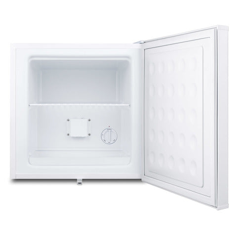 A small, white compact freezer with its door open. The interior is empty, featuring a single wire shelf and a temperature control dial on the back wall. The flat door has a textured rectangular pattern, ideal as an undercounter freezer in tight spaces.