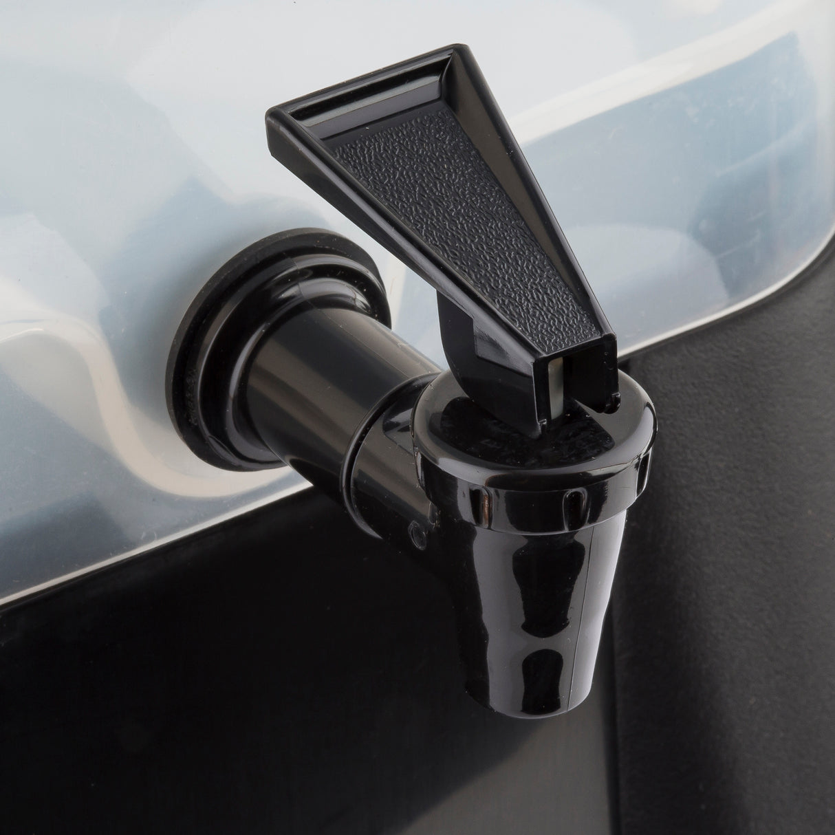 Close-up of a black plastic spigot attached to a translucent 3 gallon beverage dispenser. The spigot’s lever handle and textured details stand out against the clear container surface. The dispenser is dishwasher safe for easy cleaning.