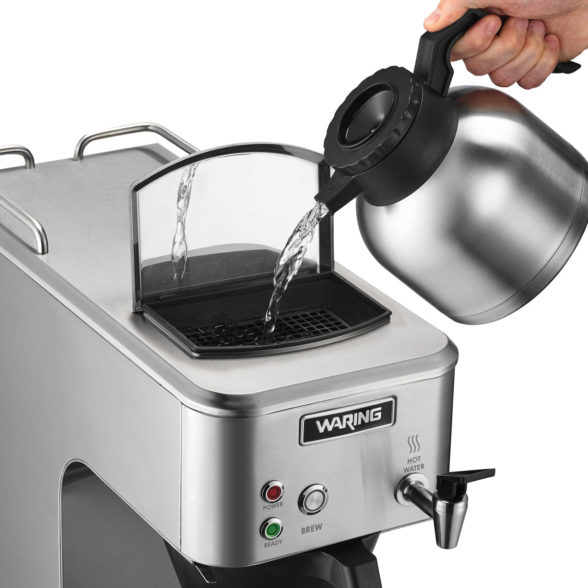 A hand pours water from a metal carafe into the open reservoir of a stainless steel commercial coffee brewer. The machine features labeled buttons for power and brew, a “hot water” spout, and a small screen covering the reservoir opening.
