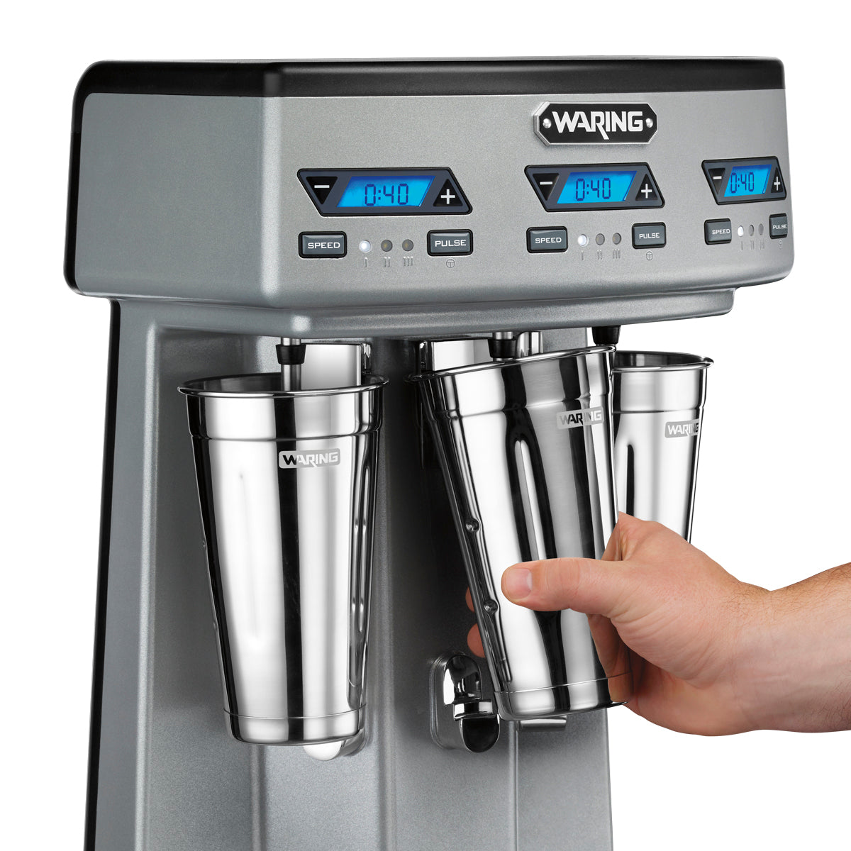A close-up of a person’s hand placing a metal mixing cup into a Waring WDM360TX Drink Mixer, featuring triple spindle stations. The shiny mixer cups and digital blue displays add prominence to this commercial-grade machine.