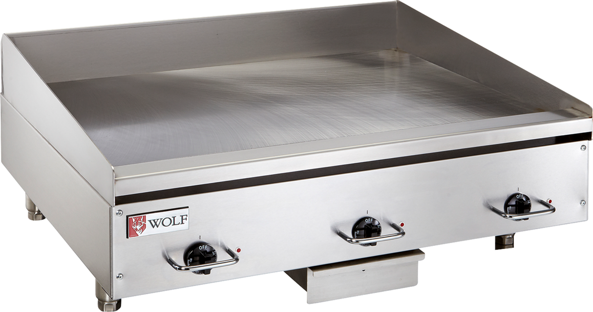A commercial electric griddle featuring three black control knobs, raised side and back splashes, and a small Wolf brand logo on the front left corner. This stainless steel griddle offers a flat cooking surface with a grease tray beneath the front edge.