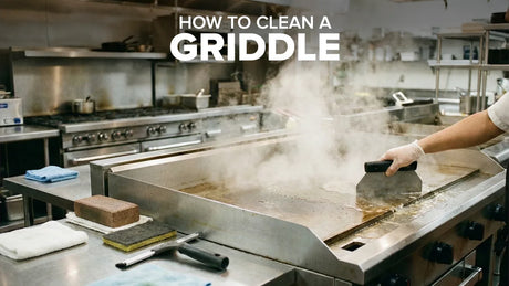 Commercial flat-top griddle being cleaned with a scraper and cleaning tools in a professional kitchen