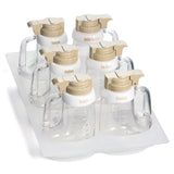 This Salad Dressing Dispenser Set features six clear dispensers with beige lids, displayed on a plastic tray. Each dispenser is labeled and has a trigger-style pour top, making it both stylish and dishwasher safe for easy cleaning.