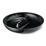 A glossy black round cat food dish, resembling a black phenolic ashtray, features a raised zigzag barrier to slow eating. The plain white background highlights the shiny surface and unique divider inside this dishwasher safe bowl.