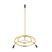 A brass plated paper towel holder from TableCraft Products with a vertical rod and three rounded legs tipped with black rubber ends. The minimal, modern design adds a sleek touch to any kitchen countertop.