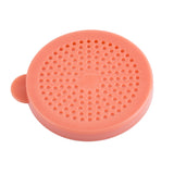 A round, flat, coral-colored silicone disk with a small tab on one side. Made from BPA free material, its surface features evenly spaced holes arranged in concentric circles—perfect for use as a dredge shaker for medium ground spices. Background is plain white.