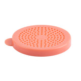 A round, flat, pink silicone drain cover with many small holes arranged in concentric circles. Featuring a small tab for easy lifting, this universal cover is dishwasher safe and photographed on a white background.