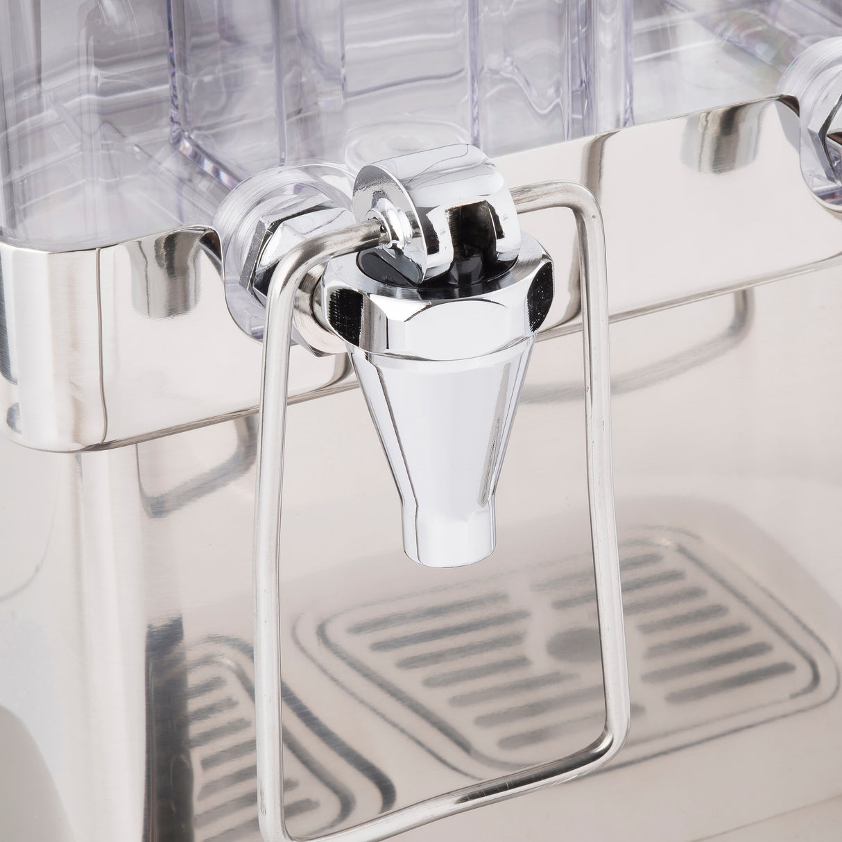 Close-up of a shiny metal beverage dispenser spigot with a lever handle, attached to a clear polycarbonate container. The reflective spout is centered above a removable drip tray with vertical slots.