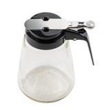 This Modern Glass Dispenser by TableCraft Products features a clear glass body with a black plastic and metal lid and lever handle for easy pouring. Dishwasher safe and empty, it's photographed on a white background from a slightly elevated angle.