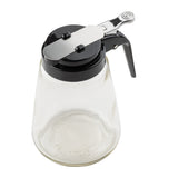 A modern glass dispenser by TableCraft Products, featuring a black plastic lid, metal lever for pouring, and integrated handle. Dishwasher safe and empty, it is shown against a white background with the lever positioned horizontally across the top.