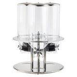 This stainless steel triple cereal dispenser features three clear polycarbonate containers, each with a silver lid and dispensing knob. Its round base and modern, polished design make it ideal for buffet or breakfast setups.