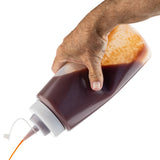 A hand squeezes a large, 32 oz WideMouth Squeeze Bottle of brown sauce, dispensing some through the nozzle. Sauce residue is visible inside the partially filled bottle, all set against a clean white background.