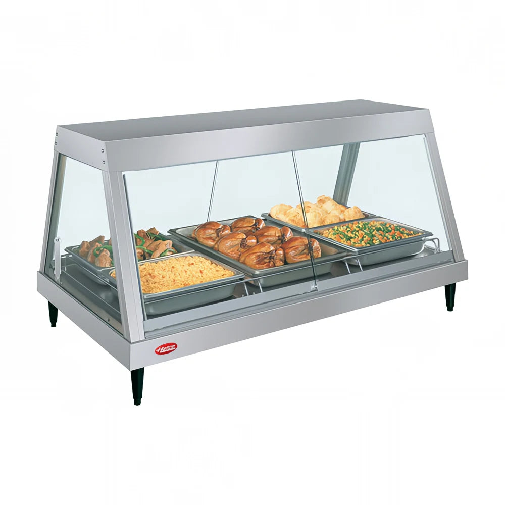 A countertop heated display case with infrared top heat features a glass front and holds four trays of food: sautéed vegetables, baked chicken, mixed vegetables, and bread rolls. It stands on four black legs with a red logo on the lower left front.