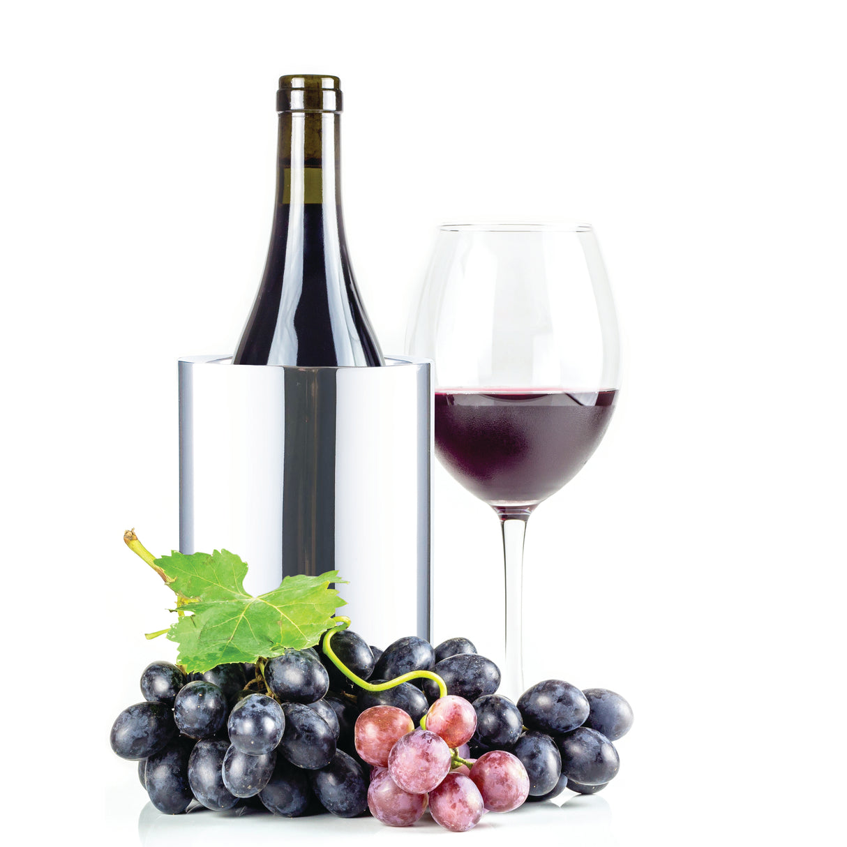 A bottle of red wine sits in a double wall stainless steel wine cooler next to a filled glass. In front, clusters of black and red grapes with a green leaf are artfully arranged, all set against a white background.