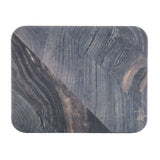 A rectangular mat with rounded corners featuring a barnwood pattern in dark shades of gray and brown. The design is split diagonally with contrasting textures, creating a modern, geometric appearance—perfect as a stylish melamine serving tray. The background is white.