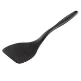 A black plastic spatula with a wide, flat, rectangular blade and a slightly curved, silicone handle. The ergonomically shaped handle features a small hole at the end for hanging. The spatula is set against a plain white background.