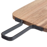 A close-up of an acacia serving paddle with a rounded edge, featuring a black metal handle attached with four screws. The rectangular handle extends outward for easy gripping or hanging, part of the industrial collection.