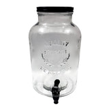 A clear glass beverage dispenser with a black screw-on lid and spigot at the bottom front. This 2 gallon beverage dispenser features embossed “Quality Beverages Est. 1924” text and laurel branches, photographed empty against a white background.