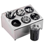 A stainless steel flatware cylinder holder keeps six black round containers filled with assorted, dishwasher safe silverware—knives, forks, and spoons. Beside it, a separate black perforated cup holds mostly forks standing upright.