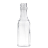 A clear, empty glass carafe with a wide base, narrow neck, and fitted glass stopper. The 1-1/2 qt cylindrical bottle curves outward at the shoulders and stands upright against a plain white background.