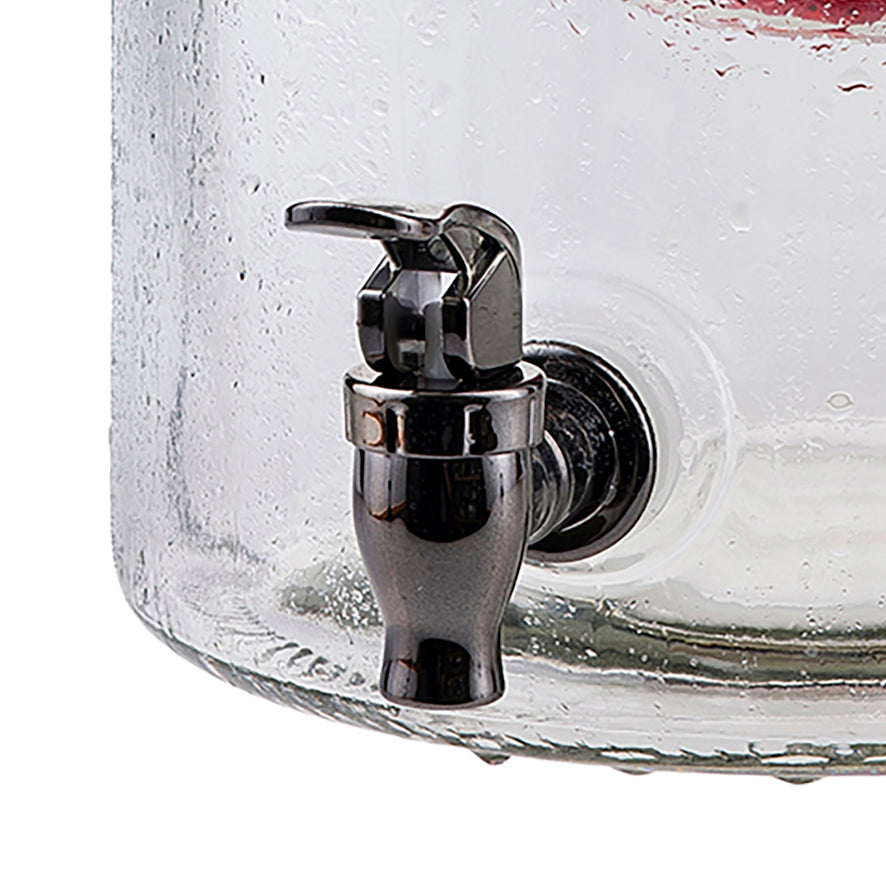 Close-up of a black plated plastic replacement faucet on a clear, textured glass beverage dispenser. The spigot is attached near the bottom, with water droplets visible on the outer surface of the glass.