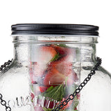 A close-up of a large TableCraft beverage dispenser with a black screw-on lid and metal chain. Inside, fresh strawberries, ice cubes, and mint leaves are visible through condensation on the cold glass surface.
