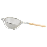 A metal mesh strainer with a double medium mesh and round bowl shape features a long, round wooden handle. It has a supporting metal ring and two prongs to rest on a bowl or pot. The background is plain white.
