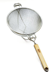 A metal mesh strainer with a round wooden handle, featuring double medium mesh for efficient straining. The strainer is angled on a white background, with support hooks opposite the handle and a hanging loop at the end.