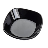 A glossy, empty TableCraft 10315BK black ceramic bowl with rounded square edges is shown against a white background. Its reflective surface creates white highlights on the inner rim. The perspective is slightly above and angled. Dishwasher safe for easy cleaning.