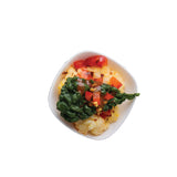 A small white mini melamine bowl filled with scrambled eggs, sautéed spinach, and diced red bell peppers. The fresh, colorful ingredients stand out against the plain background. This TableCraft 10315W bowl is also dishwasher safe.