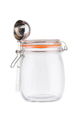 A clear resealable glass canister with a sturdy clip-top lid and orange rubber seal sits upright. A shiny metal measuring cup is attached to the canister’s side. The jar is empty and set against a white background.