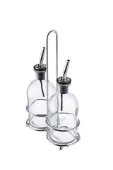 Two empty clear glass Oil & Vinegar Bottles with stainless steel pourers sit side by side in a chrome plated rack with a handle, neatly secured by metal rings at the base and around the middle.