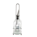 A clear glass Oil & Vinegar Bottle with a stainless steel pourer sits in a simple round chrome plated rack with a handle and four small ball feet. The bottle is empty, and the design is modern and minimalistic.