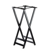 A black folding tray stand with sturdy rubberwood legs crossed in an “X” shape, featuring two flat support straps on top for holding suitcases. The structure is simple, open, and ideal for hotel rooms or guest spaces.
