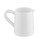 A white ceramic creamer from the Pulito Collection, featuring a rounded body, small pouring spout, and curved handle. Subtle horizontal ridges add to its simple, clean, and modern design against a plain white background.