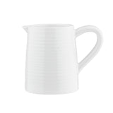 A white ceramic creamer from the Pulito Collection, featuring a ribbed texture, small left spout, and curved right handle. Simple and unadorned, it’s set against a plain white background.