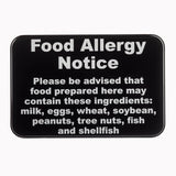 A wall mounted black warning sign with bold white text reads: Food Allergy Notice. Please be advised that food prepared here may contain these allergy ingredients: milk, eggs, wheat, soybean, peanuts, tree nuts, fish, and shellfish.