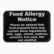 A wall mounted black warning sign with bold white text reads: Food Allergy Notice. Please be advised that food prepared here may contain these allergy ingredients: milk, eggs, wheat, soybean, peanuts, tree nuts, fish, and shellfish.