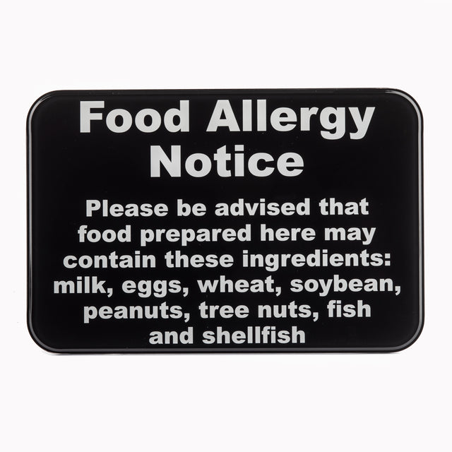 A wall mounted black warning sign with bold white text reads: Food Allergy Notice. Please be advised that food prepared here may contain these allergy ingredients: milk, eggs, wheat, soybean, peanuts, tree nuts, fish, and shellfish.