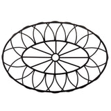 A black, oval-shaped metal trivet from the TableCraft Petal Collection features a geometric, symmetrical pattern with radiating petal-like shapes. Its flower-like design and open structure make it a stylish pairing with any metal oval basket.