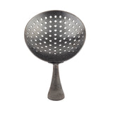 A perforated metal ladle, resembling a Julep Strainer, features a wide, round bowl with evenly spaced holes and a short handle. Its textured surface and black acid etch finish evoke the look of dark, aged metal against a white background.
