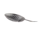 A stainless steel Julep Strainer with a round, shallow, perforated bowl and a slightly curved handle extends to the right. Its textured surface and multiple circular holes allow for efficient draining, while the black acid etch finish adds a modern touch.