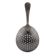 A vintage stainless steel slotted spoon with a wide, slightly oval bowl featuring multiple round holes for draining and a textured, curved handle that tapers at the end. The metal has a dark, matte black acid etch finish. Shown on a white background.