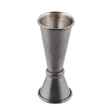 A stainless steel Japanese Jigger with a textured, hammered surface. It features two cone-shaped measuring cups joined at the base, one larger and one smaller, used for measuring liquor when making cocktails. The jigger is silver in color and stands upright.