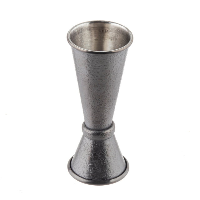 A stainless steel Japanese Jigger with a textured, hammered surface. It features two cone-shaped measuring cups joined at the base, one larger and one smaller, used for measuring liquor when making cocktails. The jigger is silver in color and stands upright.