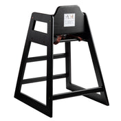 A stackable black wood restaurant-style high chair featuring an open-frame design, safety strap, and warning label on the backrest. Angled for stability, it's perfect for seating young children at tables.