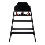 A stackable black high chair with a minimalist design, viewed from the front. It features a wide, sturdy wood base and angled legs. Two red safety straps are attached to the tall, solid backrest, all set against a plain white background.