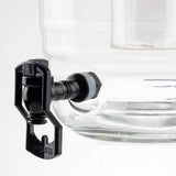 Close-up of a clear glass beverage dispenser with a black plastic spigot, similar to some Universal Touchless Faucet designs, featuring a lever labeled PUSH. Set against a plain white background, the dispenser stands out prominently.