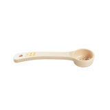 A beige perforated polycarbonate spoon with a long handle and round bowl, featuring small drainage holes in the bottom. "Spoonout" is written in yellow on the handle. The background is plain white.