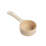 A beige polycarbonate measuring cup with a long handle. The cup is perforated with small drainage holes at the bottom for liquid to pass through. Blue measurement markings indicate 8 OZ and 240 ML. The Spoonout cup is set against a white background.